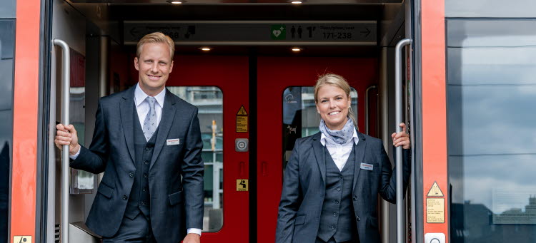 Två tågvärdar som tittar ut genom dörröppningen på tåget..